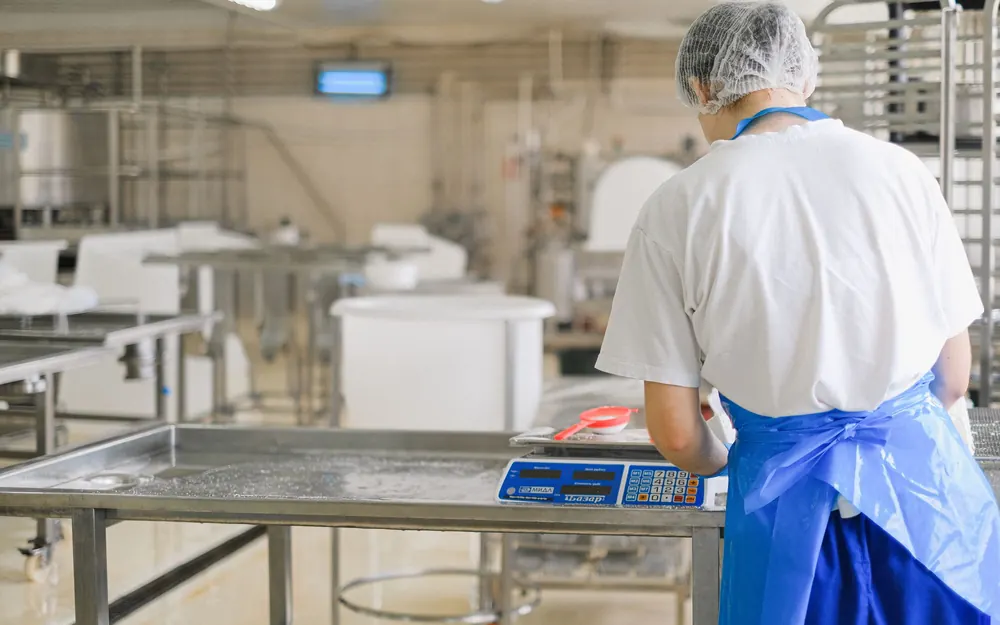 Worker in hairnet and apron weighing product on a digital scale